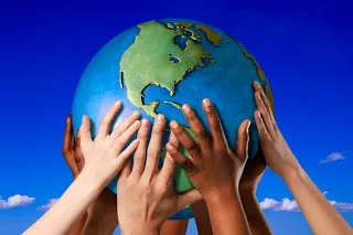 Multiple diverse hands holding globe together against blue sky background, symbolizing global unity and teamwork.