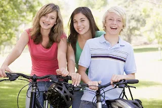 Three women of different ages holding bicycles outdoors in a park setting.