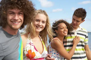 Four smiling teenagers outdoors enjoying summer day together in casual clothing.
