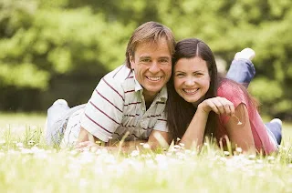 Happy family lying on grass outdoors, smiling together in park setting.