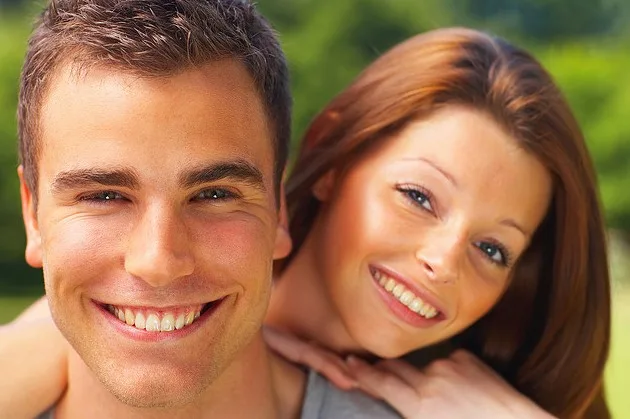 Young couple smiling outdoors with healthy teeth and bright expressions in natural daylight setting.