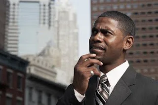 Professional man in business suit thinking thoughtfully against urban cityscape backdrop.