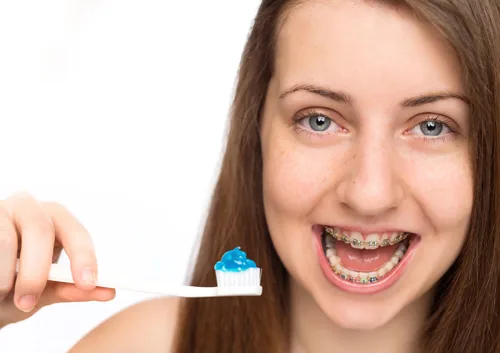 Young woman smiling brightly while holding toothbrush with toothpaste, promoting dental care and orthodontics.