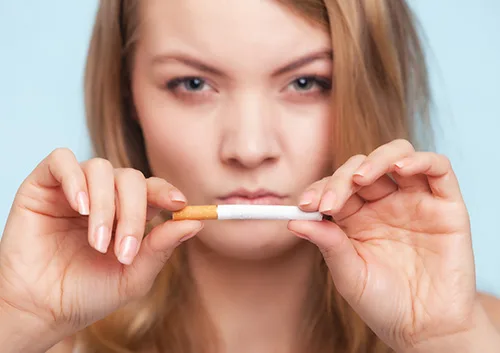 Woman breaking cigarette in half against light blue background, symbolizing smoking cessation