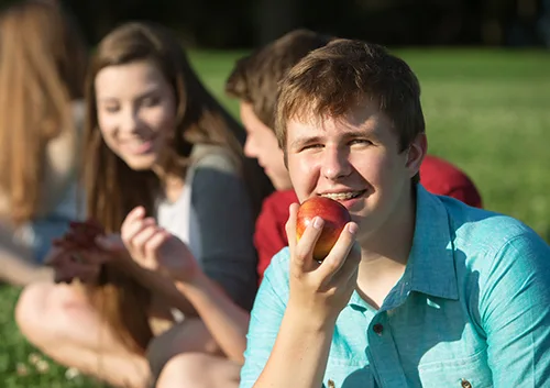 Young boy eating apple with family sitting on grass outdoors
