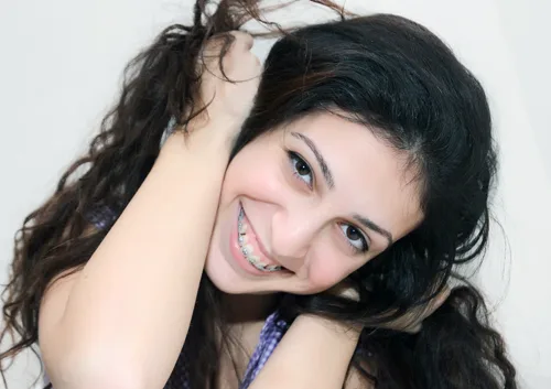 Young woman smiling at camera, touching her hair, wearing blue lanyard against white background.