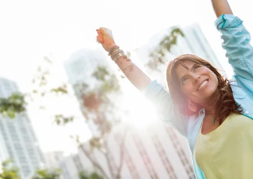 Woman and child with arms raised celebrating outdoors in sunny residential setting.