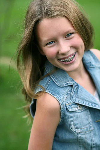 Smiling girl wearing denim shirt against green background, showcasing healthy teeth and braces results.
