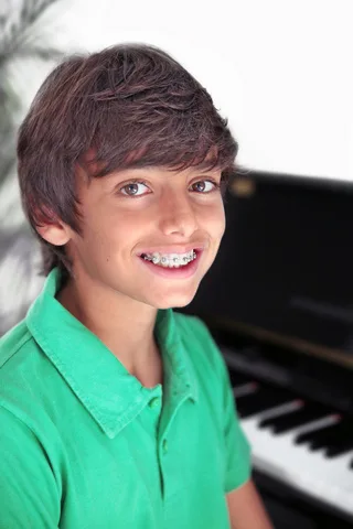 Young boy in green shirt smiling at camera with piano in background.