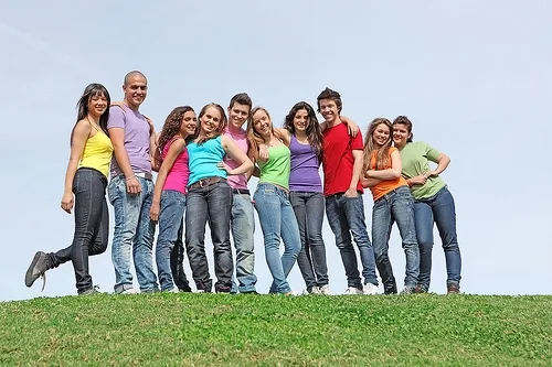 Group of smiling children standing together on grass against blue sky.
