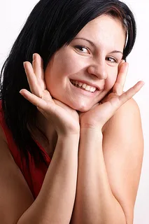 Smiling woman with hands to face in red top against white background
