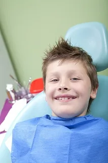 Young boy smiling in dental chair wearing blue bib at orthodontics office