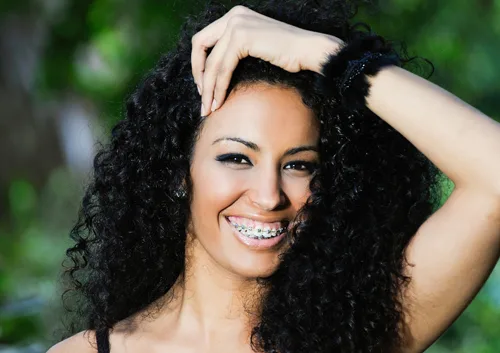 Smiling woman with curly black hair showcasing bright teeth against blurred green background.