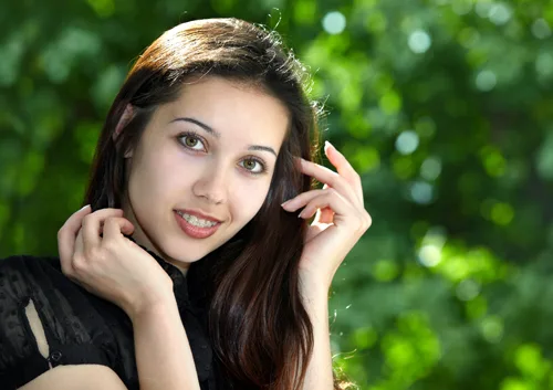 Young woman smiling at camera with hands near face, green foliage background