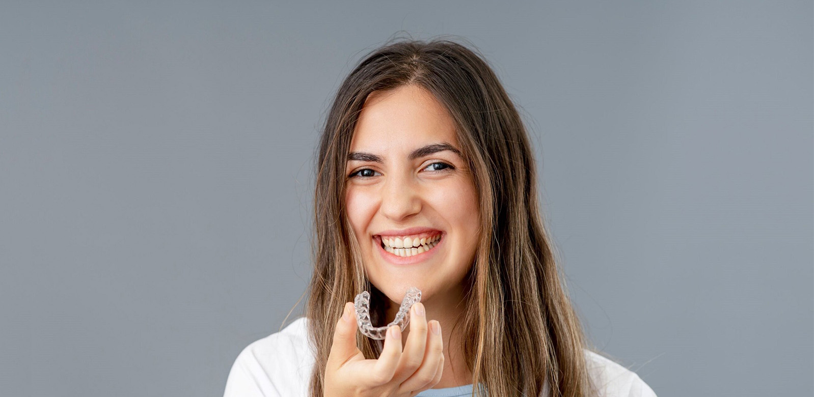 Woman smiling at camera wearing white shirt against gray background, professional headshot style portrait
