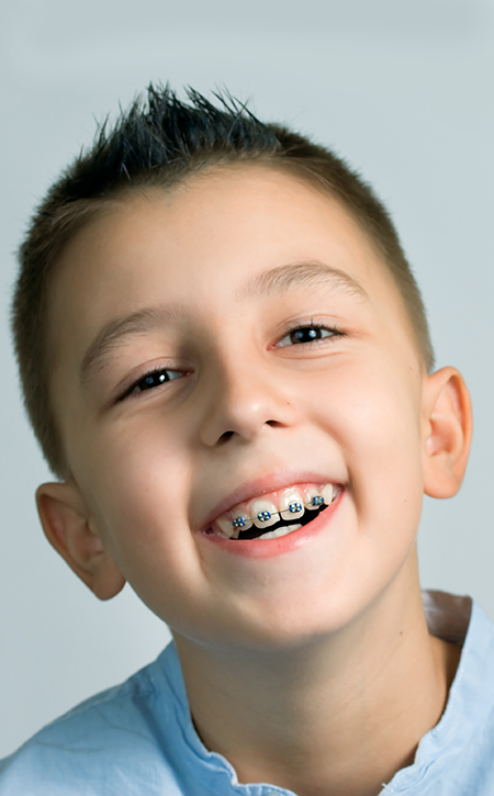 Young boy smiling at camera wearing blue shirt against light blue background