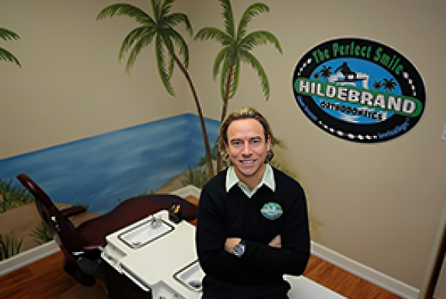 Professional man in dark blazer sits at desk in orthodontics office with Hildebrand logo visible.