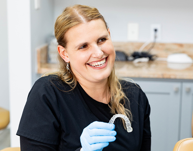 Smiling dental professional in black shirt wearing blue gloves in modern orthodontic office kitchen.