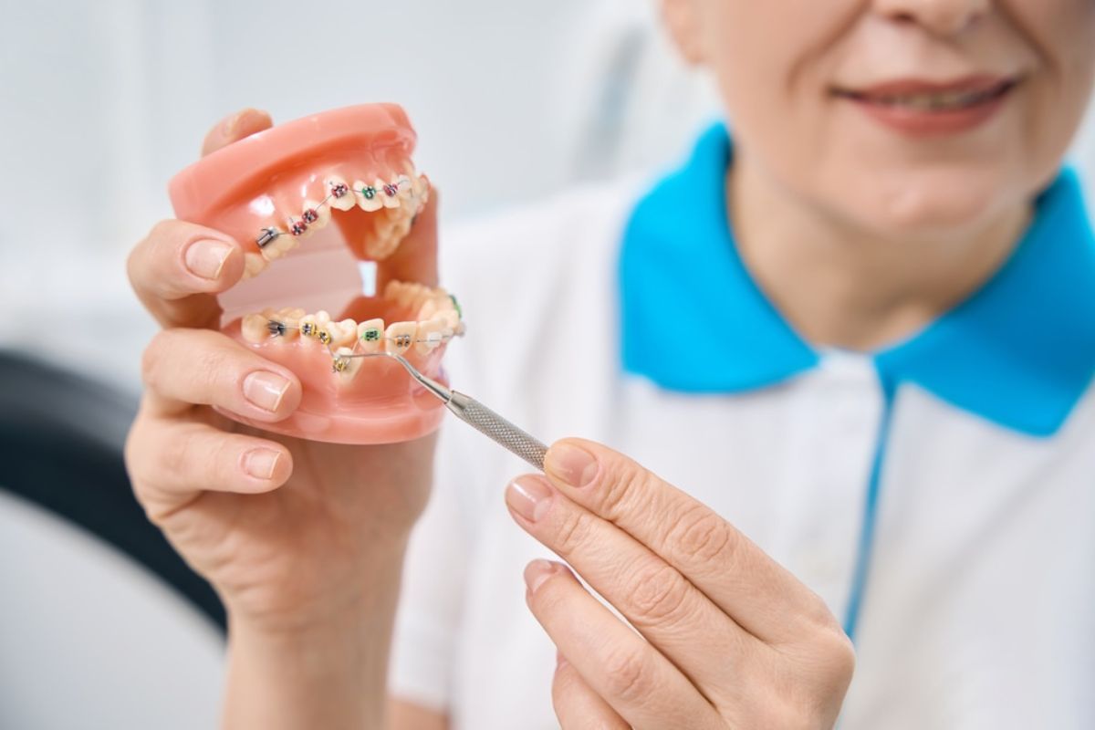 Orthodontist demonstrating dental braces model to patient in clinical office setting.