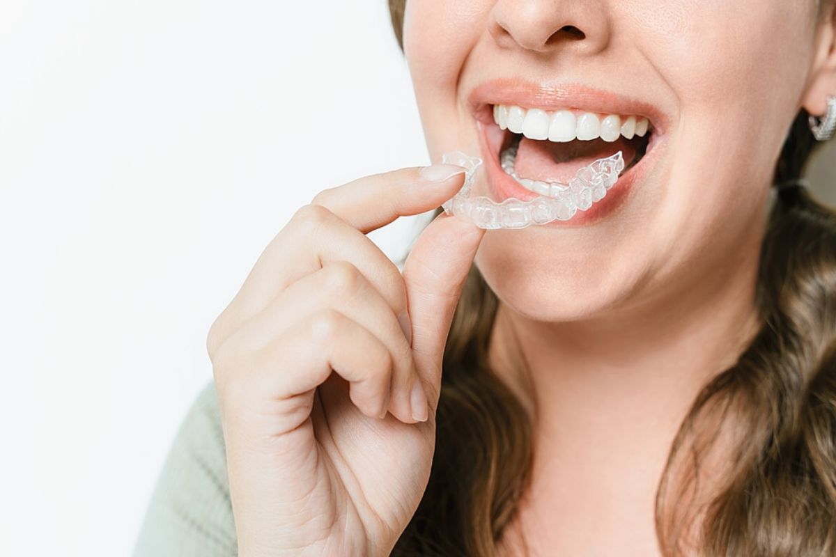 Woman smiling brightly while pointing to her straight white teeth against white background.