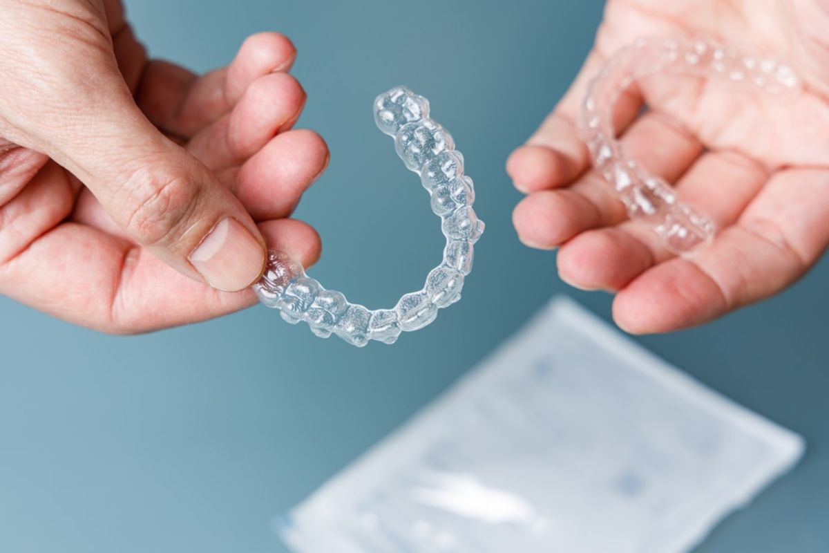 Hands holding clear orthodontic aligner tray against blue background with case below.