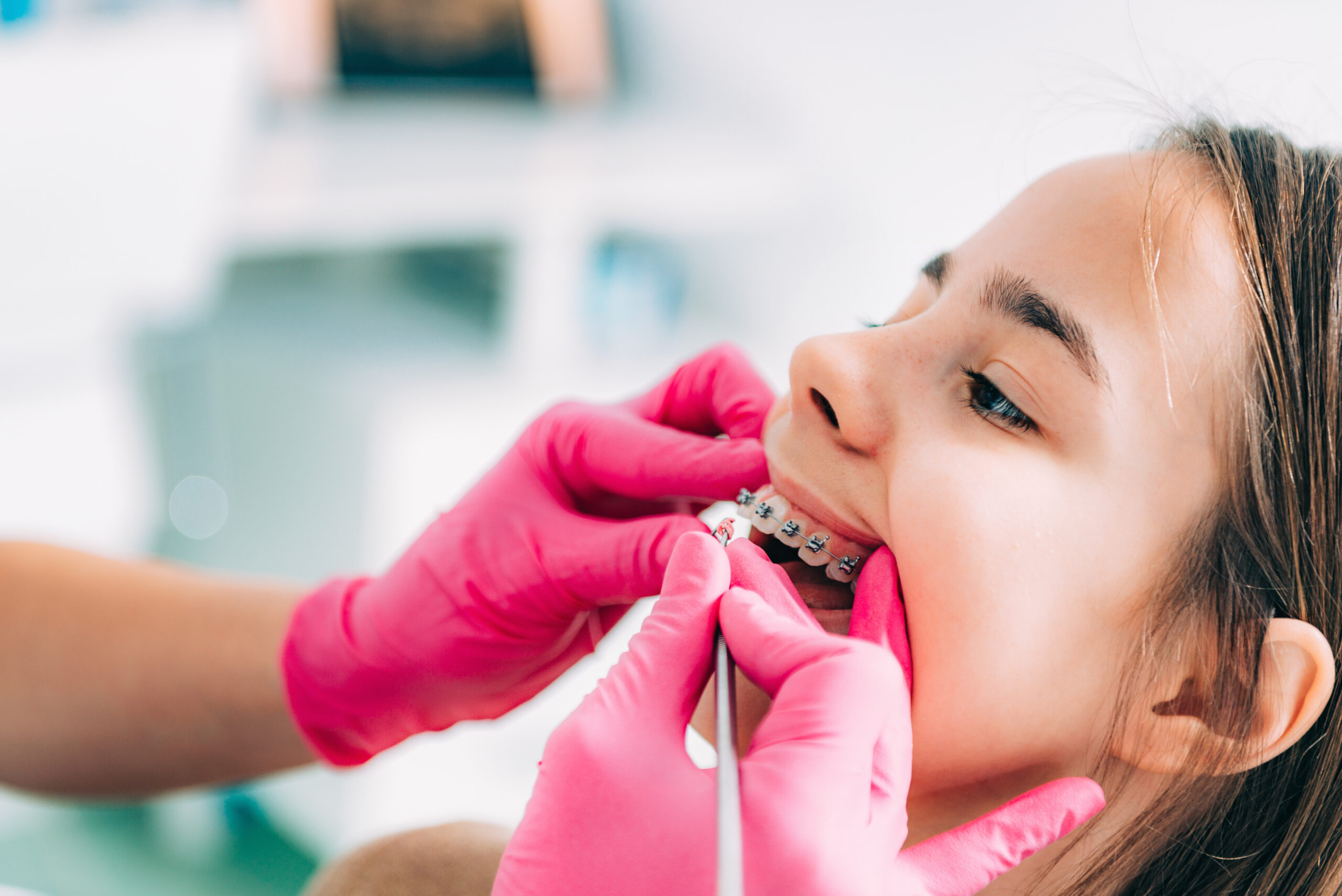Young patient receiving orthodontic treatment with braces adjustment by dental professional in pink gloves.
