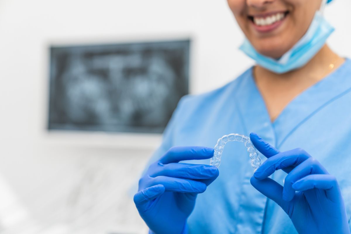 Orthodontist holding clear aligner tray with dental X-rays visible in background.